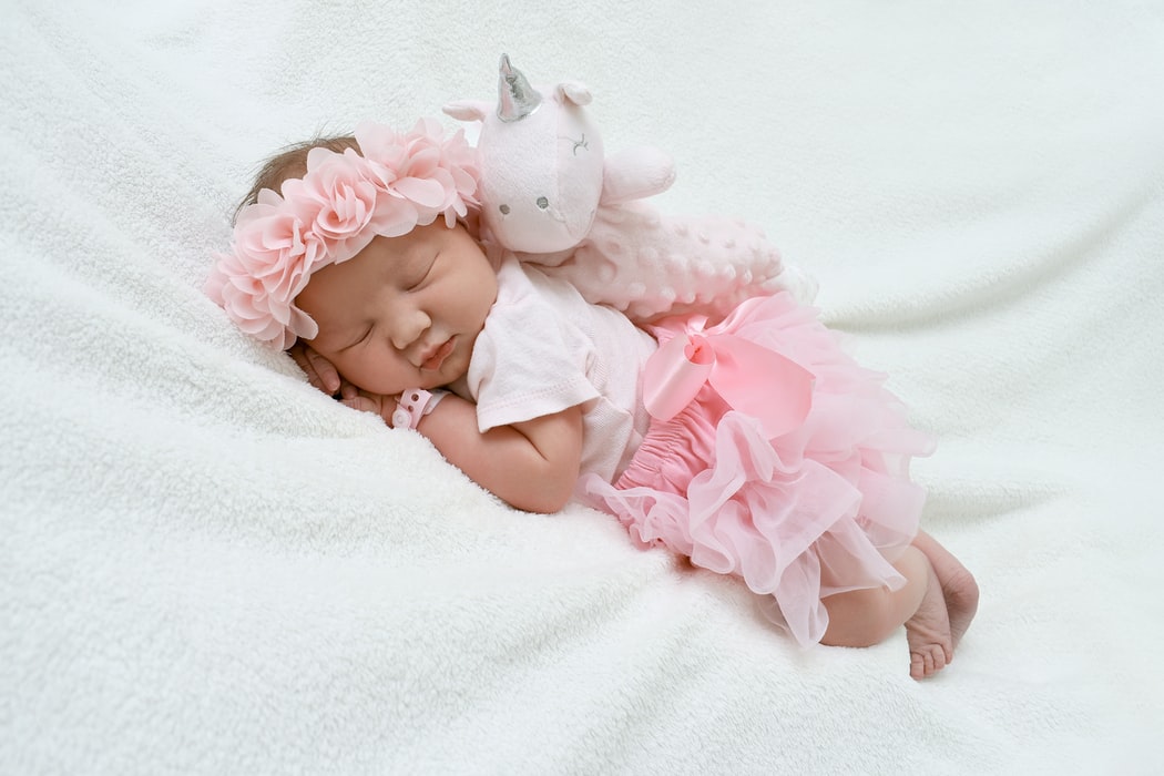 sleeping infant with pink tutu and pink flower headband on white blanket