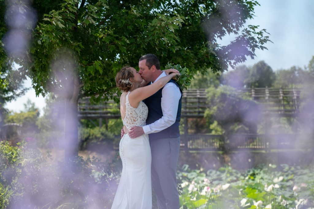 Photogenic pose, intimate moment, groom holding bride’s waist and kissing under a long veil